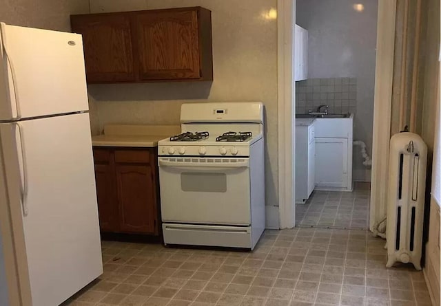 kitchen featuring white appliances, radiator heating unit, light countertops, and a sink
