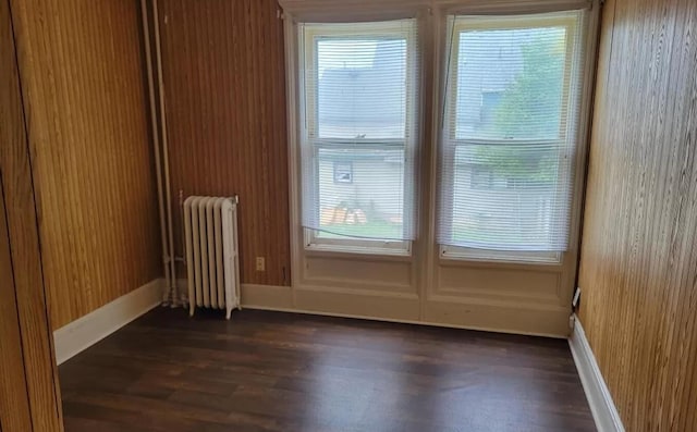 spare room with radiator, dark wood-style flooring, and baseboards