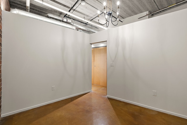 spare room featuring baseboards, finished concrete flooring, and a chandelier