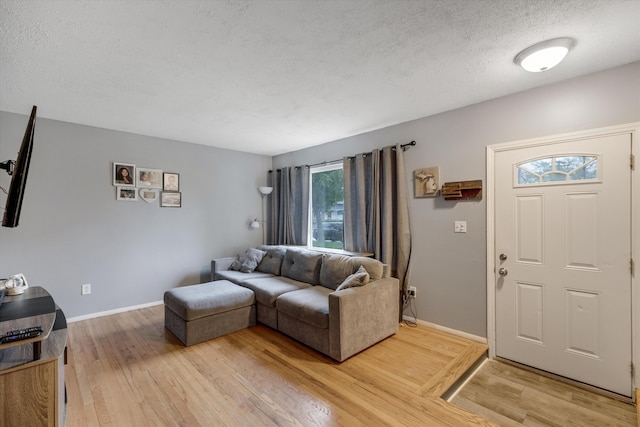 living room featuring a textured ceiling, light wood-type flooring, and baseboards