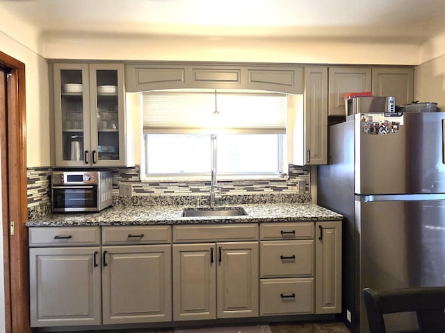 kitchen featuring freestanding refrigerator, gray cabinets, a sink, and backsplash