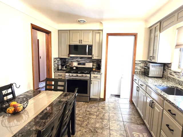 kitchen featuring appliances with stainless steel finishes, a sink, decorative backsplash, and light stone counters