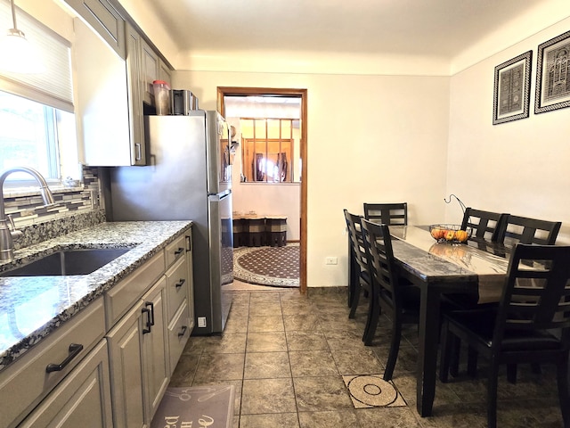 kitchen featuring a sink, decorative backsplash, light stone countertops, and gray cabinets