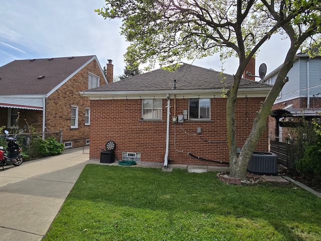 back of house featuring a yard, brick siding, central air condition unit, a chimney, and a shingled roof