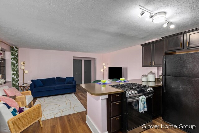 kitchen featuring freestanding refrigerator, gas range, a peninsula, open floor plan, and a textured ceiling