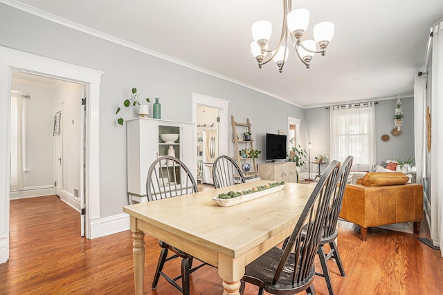 dining room featuring light wood-style floors, a chandelier, ornamental molding, and baseboards