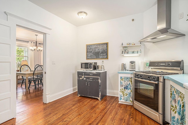 kitchen with wall chimney exhaust hood, appliances with stainless steel finishes, a chandelier, wood finished floors, and baseboards