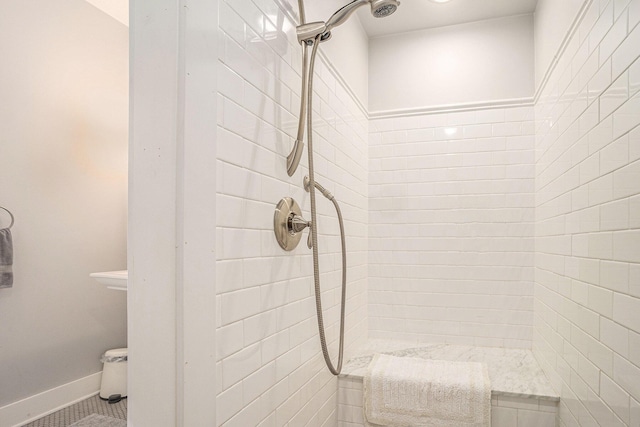 full bathroom with a tile shower and baseboards