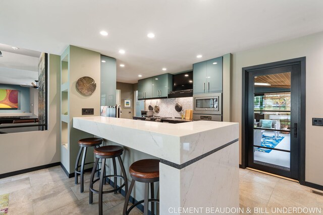 kitchen featuring stainless steel microwave, backsplash, a breakfast bar area, baseboards, and recessed lighting