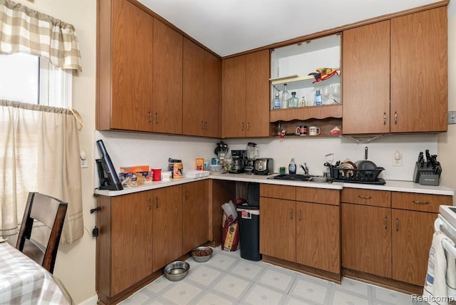 kitchen with a sink, light countertops, light flooring, brown cabinets, and white range with electric stovetop