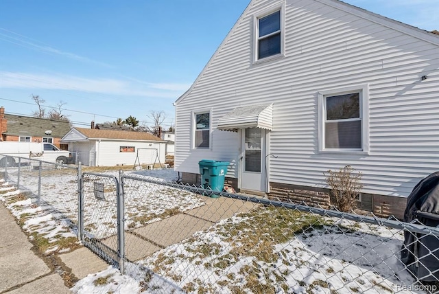 snow covered house featuring a gate and fence