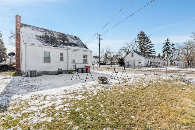 snow covered back of property featuring a chimney, fence, and central AC unit
