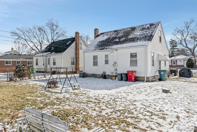 snow covered rear of property featuring fence, central AC unit, and a chimney