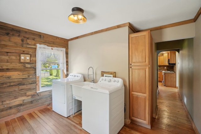 laundry room featuring washer and clothes dryer, arched walkways, light wood-type flooring, wood walls, and cabinet space