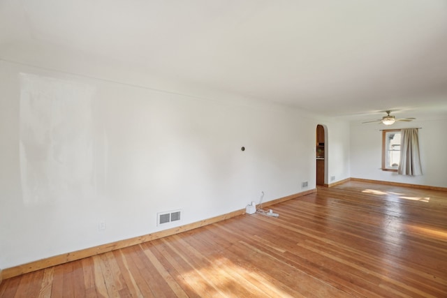 unfurnished room featuring arched walkways, hardwood / wood-style flooring, baseboards, and a ceiling fan