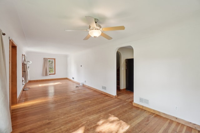 unfurnished living room featuring arched walkways, a ceiling fan, hardwood / wood-style flooring, and baseboards