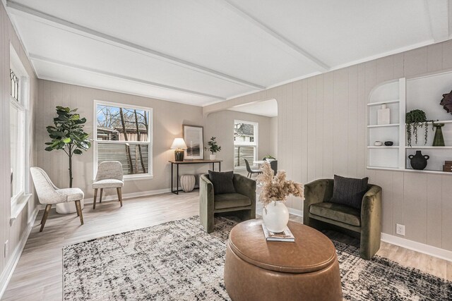 sitting room featuring healthy amount of natural light, light wood-type flooring, beam ceiling, baseboards, and wood walls