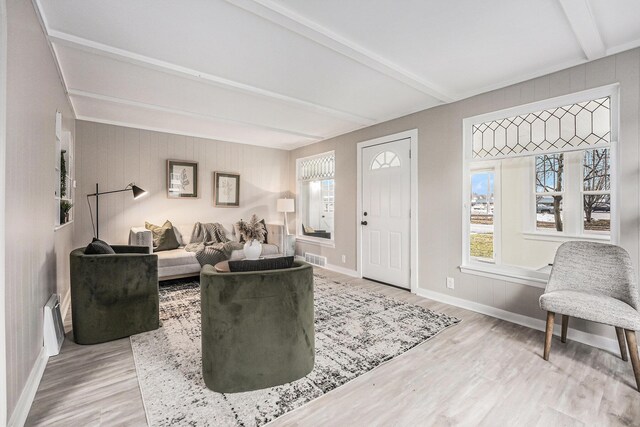 living area featuring beam ceiling, light wood-type flooring, healthy amount of natural light, baseboards, and wooden walls