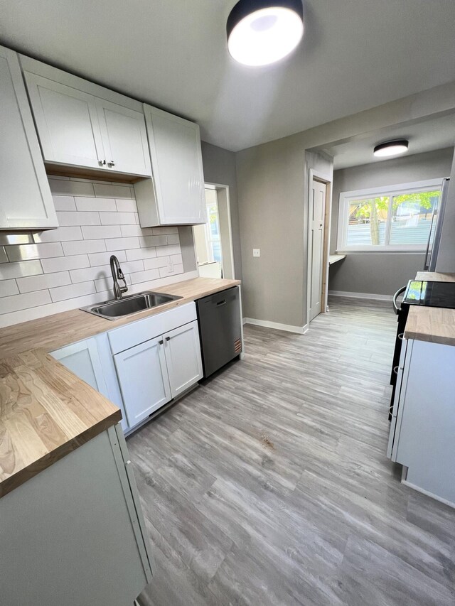 kitchen featuring stainless steel dishwasher, wooden counters, a sink, tasteful backsplash, and baseboards