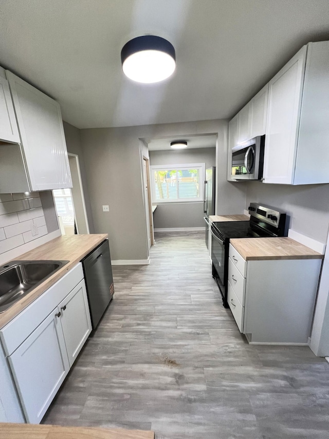 kitchen with appliances with stainless steel finishes, baseboards, a sink, backsplash, and white cabinets