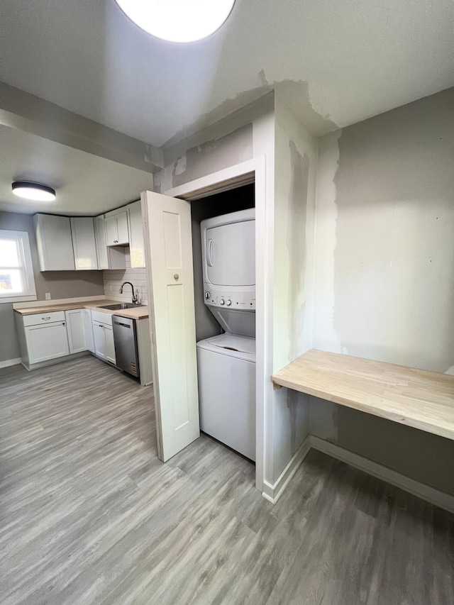 laundry area with stacked washer / drying machine, light wood-style floors, and baseboards