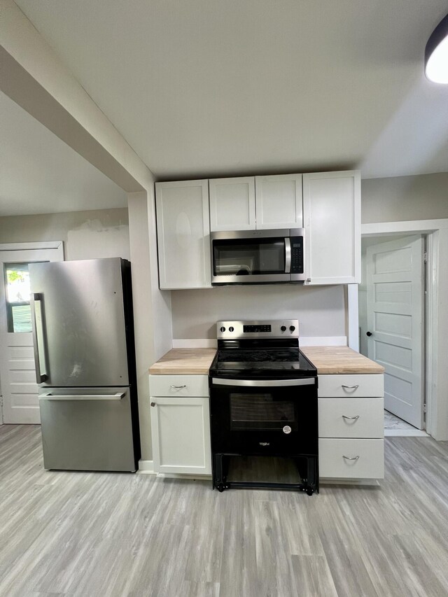 kitchen with appliances with stainless steel finishes, wooden counters, light wood-type flooring, and white cabinetry