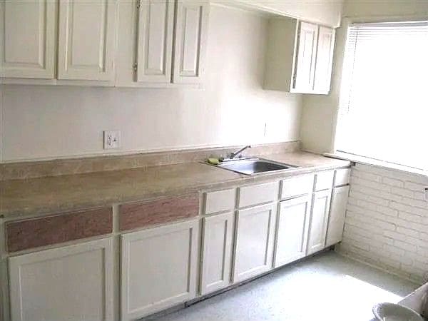 13892 Eastburn St, Detroit, MI 48205 - kitchen with a sink, light countertops, white cabinets, and brick wall