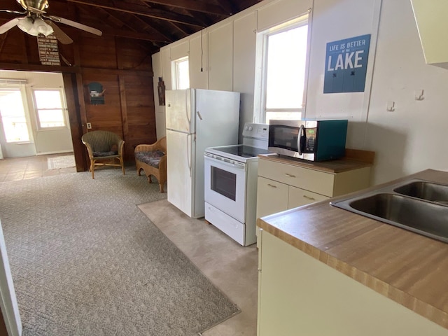 kitchen featuring white appliances, ceiling fan, white cabinets, a sink, and wooden walls