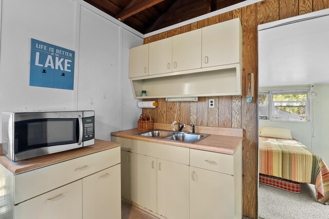 kitchen featuring stainless steel microwave, open shelves, a sink, light countertops, and beam ceiling