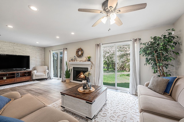 living room featuring a warm lit fireplace, light wood-style flooring, recessed lighting, and a ceiling fan