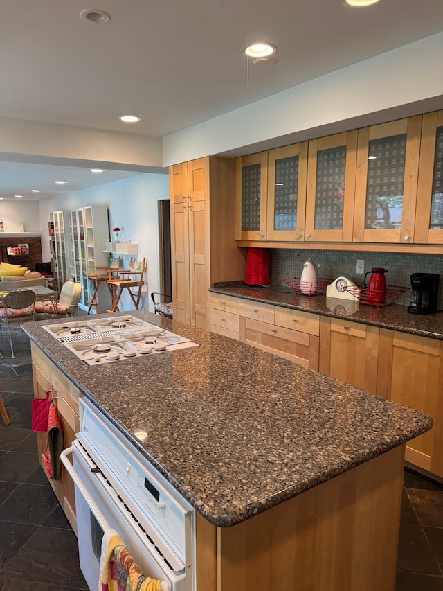 kitchen with a center island, white appliances, glass insert cabinets, recessed lighting, and dark stone counters