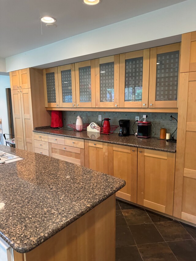 kitchen with tasteful backsplash, glass insert cabinets, and dark stone countertops