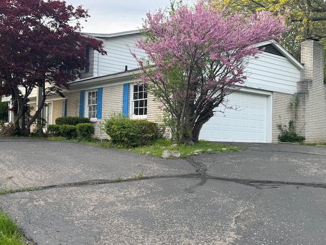 view of front of house featuring brick siding, driveway, and a chimney
