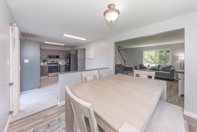 dining space featuring stairs, light wood-type flooring, and baseboards