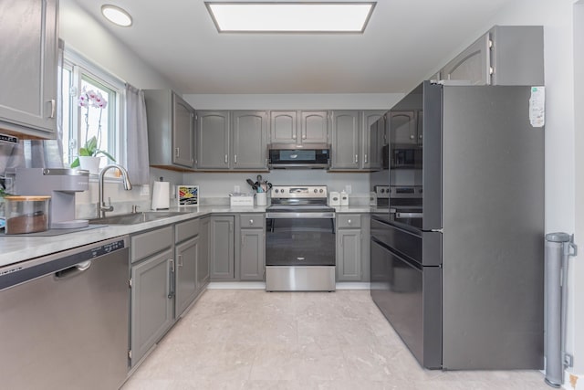 kitchen with appliances with stainless steel finishes, a sink, gray cabinets, and light countertops