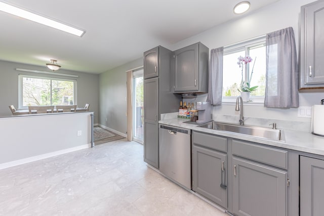 kitchen featuring stainless steel dishwasher, gray cabinets, a sink, and light countertops