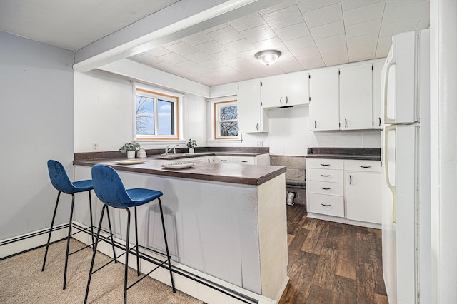 kitchen with dark countertops, a peninsula, dark wood-type flooring, freestanding refrigerator, and white cabinets
