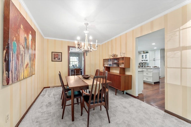 carpeted dining area with wallpapered walls, a chandelier, crown molding, and baseboards