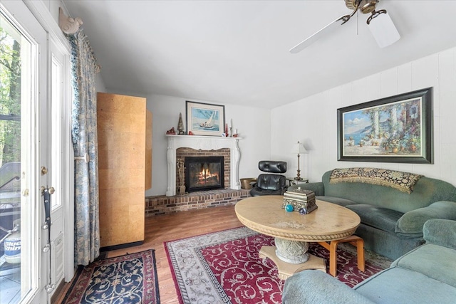 living area featuring wood finished floors, ceiling fan, and a brick fireplace