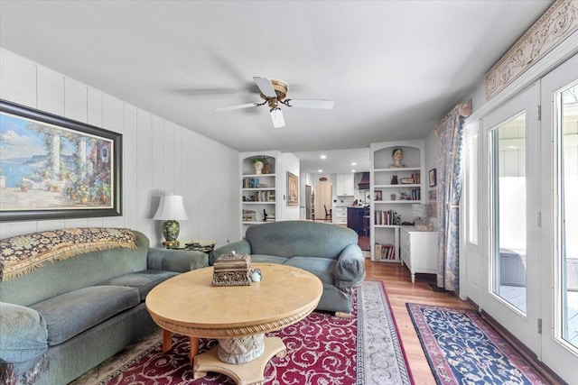 living area featuring light wood-style flooring, a ceiling fan, and built in shelves