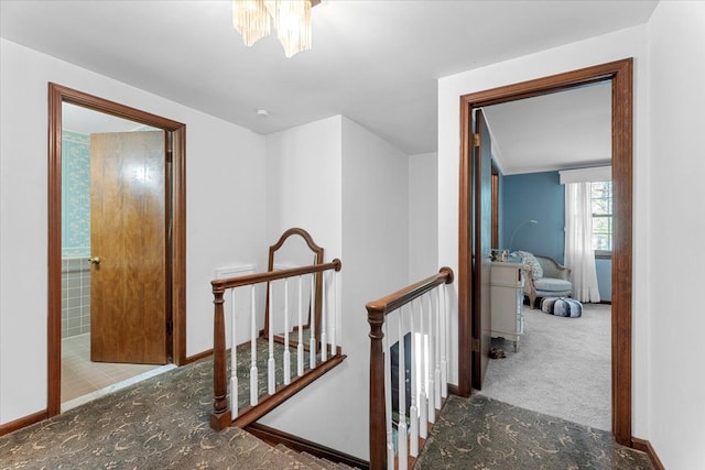 hallway with an upstairs landing, a chandelier, carpet, and baseboards