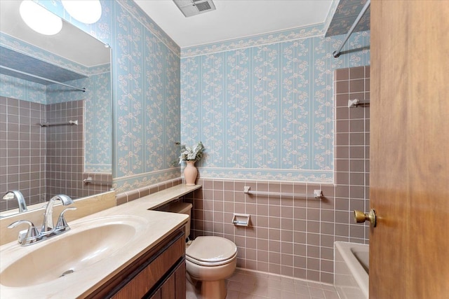 bathroom with wallpapered walls, toilet, wainscoting, vanity, and tile patterned floors
