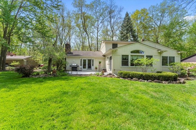rear view of property featuring a chimney, a yard, french doors, and a patio