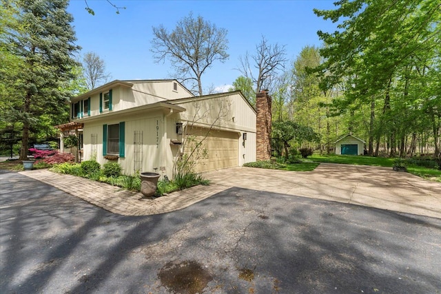 view of side of home featuring a chimney, an attached garage, and driveway