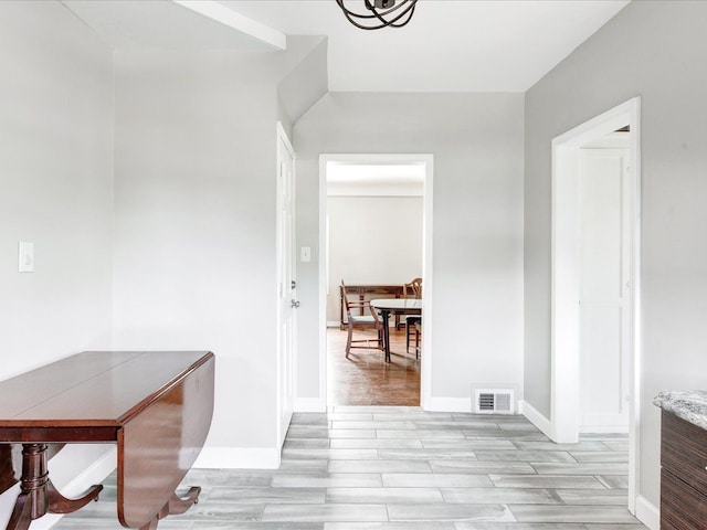 hallway featuring light wood finished floors, a chandelier, and baseboards