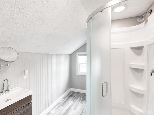 full bathroom with a textured ceiling, a stall shower, wood finished floors, vaulted ceiling, and baseboards