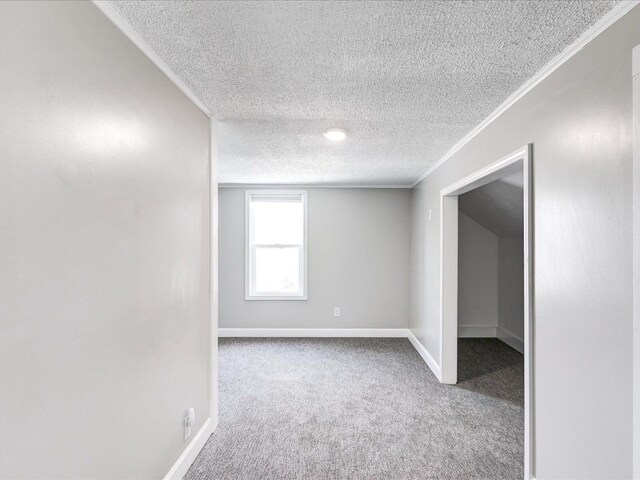 spare room with a textured ceiling, carpet, crown molding, and baseboards