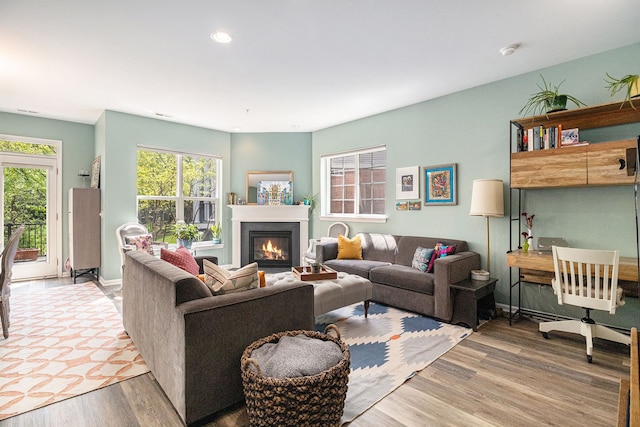 living area with a glass covered fireplace, wood finished floors, recessed lighting, and baseboards