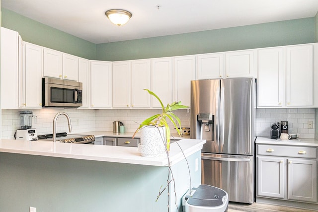 kitchen featuring appliances with stainless steel finishes, decorative backsplash, light countertops, a peninsula, and white cabinets