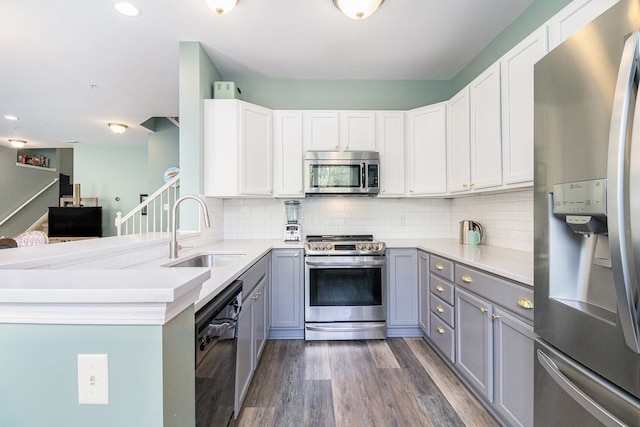 kitchen with stainless steel appliances, gray cabinets, a sink, wood finished floors, and recessed lighting